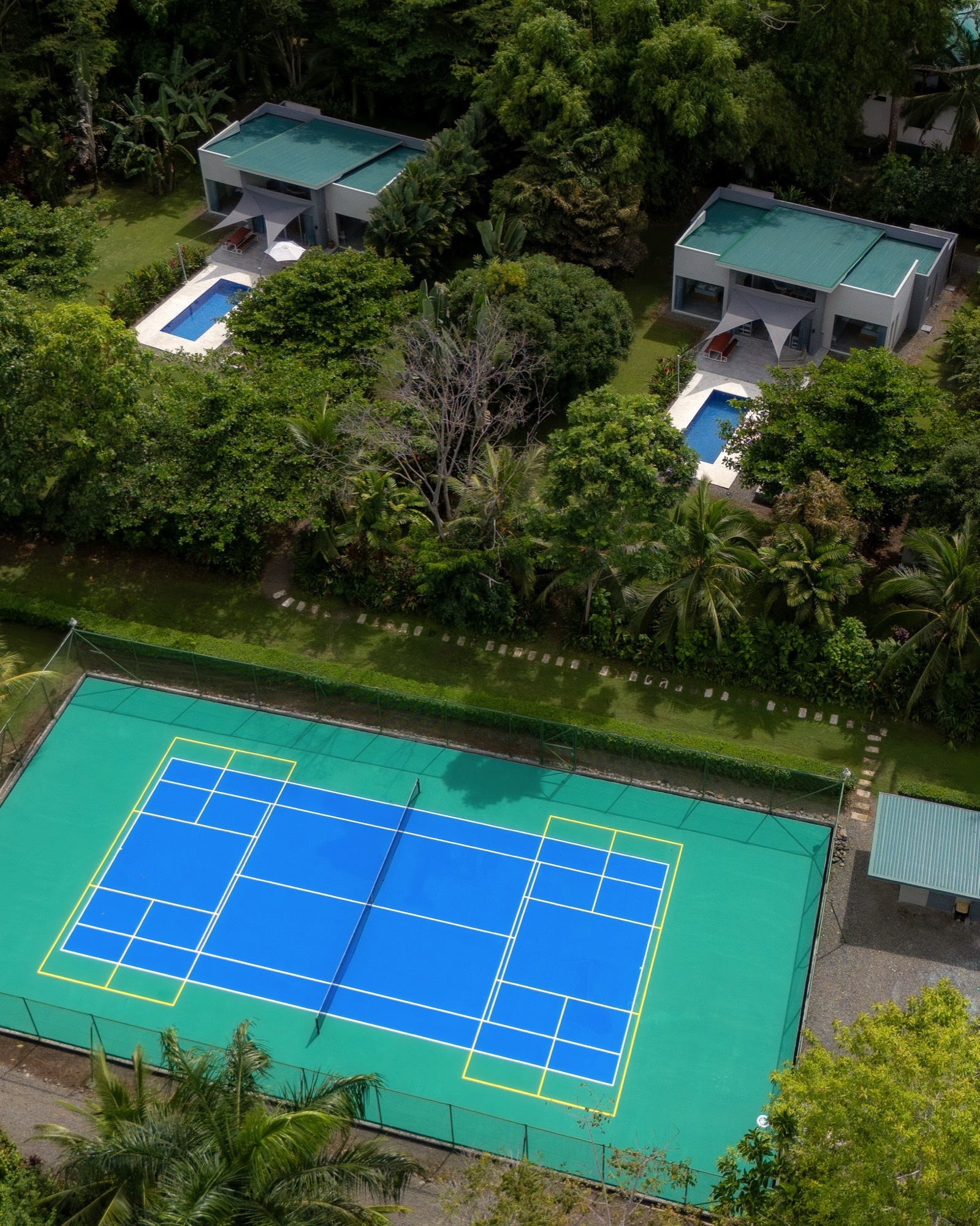 Le court de tennis et de pickleball vu du ciel, les deux maisons derrière dans la forêt